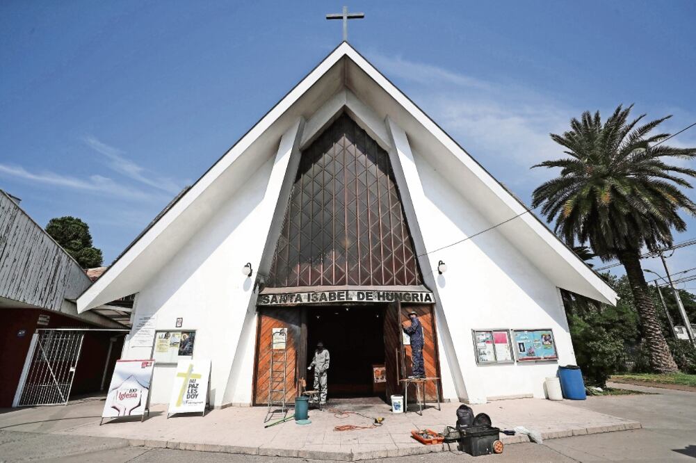 Personas trabajaban ayer en la parroquia Santa Isabel de Hungría, en donde vándalos lanzaron un paño impregnado con combustible y luego le aplicaron fuego, provocando un incendio que fue controlado por los bomberos en Santiago. (MARIO RUIZ. EFE)