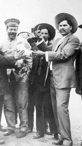 Doroteo Arango, mejor conocido como Pancho Villa, portando uniforme militar; a la derecha está uno de los Dorados de élite fiel a Villa: Rodolfo Fierro, quien enseña a la cámara la navaja que se le pondrá al gallo que alguien sostiene frente a él. Imagen de 1914. Foto: ESPECIAL/Cortesía de Mario Alberto Trillo Corral.