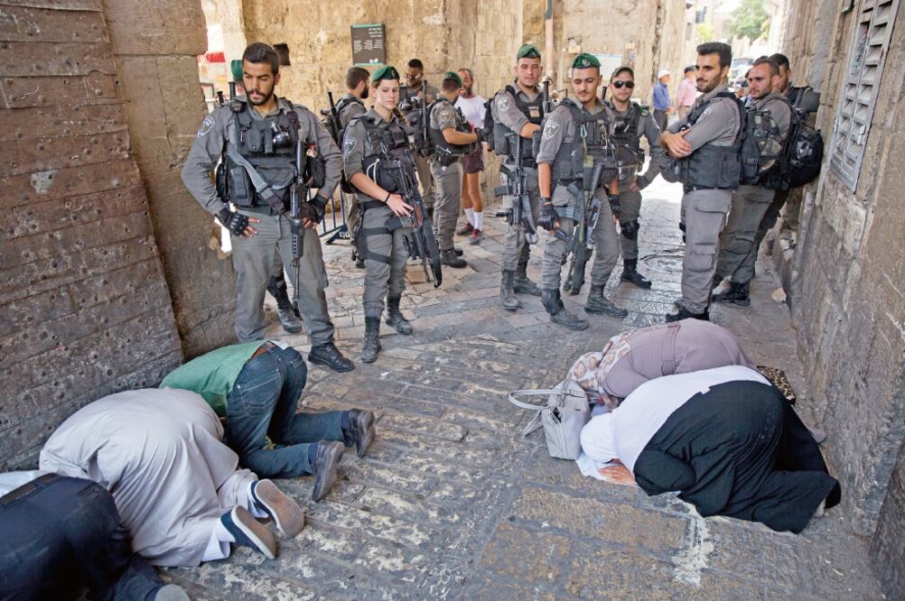 Palestinos rezan mientras la policía fronteriza israelí vigila la entrada de la Puerta del León, en la Vieja Ciudad de Jerusalén. (ODED BALILTY. AP)