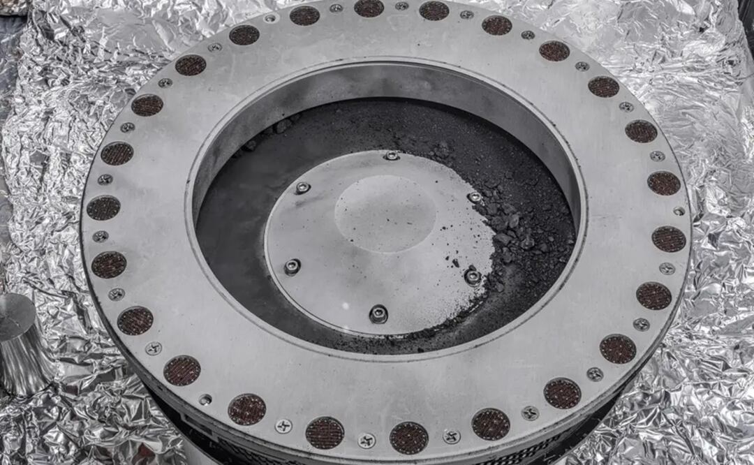 Fotografía cedida por la NASA de una vista del exterior del recolector de muestras de Osiris-Rex donde se puede ver en el centro a la derecha de la imagen parte del material traído como muestra del asteroide Bennu. Foto: EFE