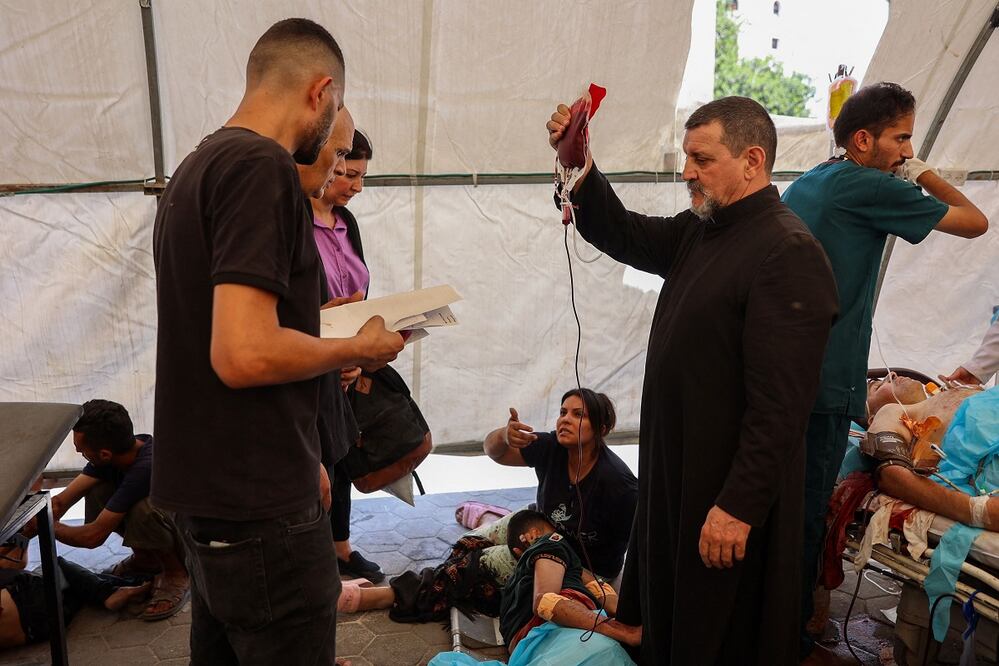 El padre Carlos (centro) de la Iglesia de la Sagrada Familia, en Gaza, auxilia a los heridos por un ataque israelí, que fueron trasladados al hospital Ahli. FOTO: OMAR AL-QATTAA. AFP
