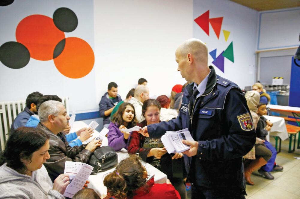 Un oficial entrega a refugiados, en Mainz, información sobre el comportamiento que se espera de ellos en el carvanal de Colonia. Autoridades prometieron ayer unas festividades seguras (KAI PFAFFENBACH. REUTERS)