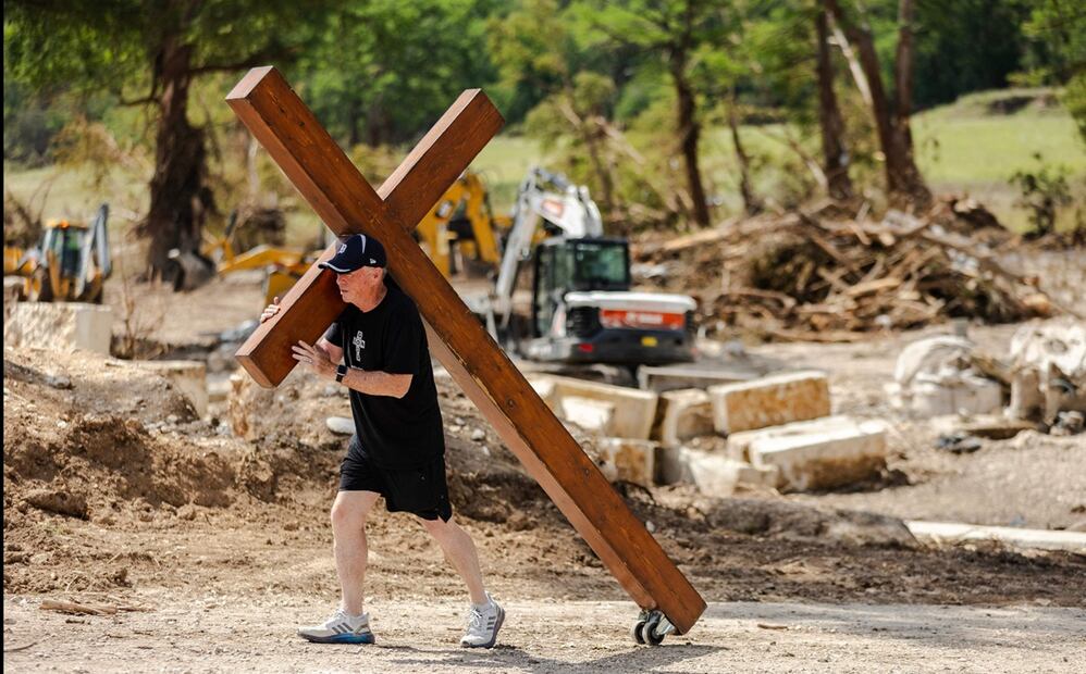Un hombre camina por la orilla del río Guadalupe cargando una gran cruz de madera en Ingram, Texas, el 8 de julio de 2025. Foto: AFP