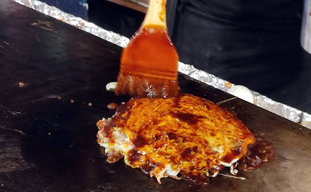Una vez que todos los ingredientes se cocieron, voltean el preparado de modo que la masa queda hacia arriba y la barnizan con la salsa okonomi. Foto: Raúl Fontecilla/EL UNIVERSAL.