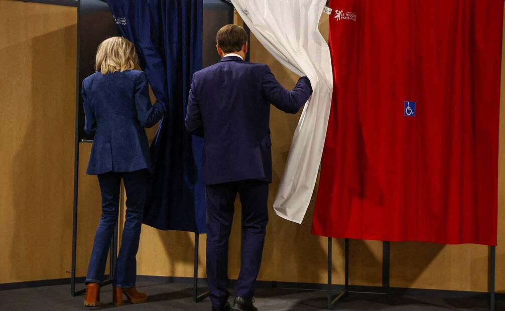 El presidente de Francia, Emmanuel Macron y su esposa, Brigitte Macron, entran en una cabina electoral. Foto: AFP