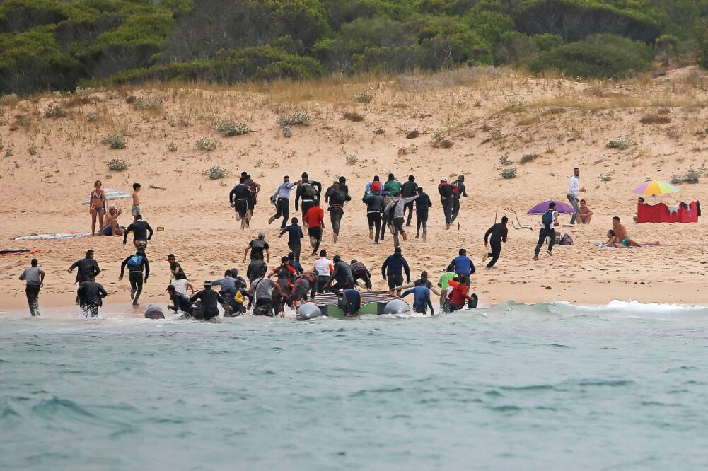 Decenas de migrantes procedentes de África corren tierra adentro en la playa española de El Cañuelo, después de atravesar el Estrecho de Gibraltar en una lancha, desde Marruecos. (REUTERS)