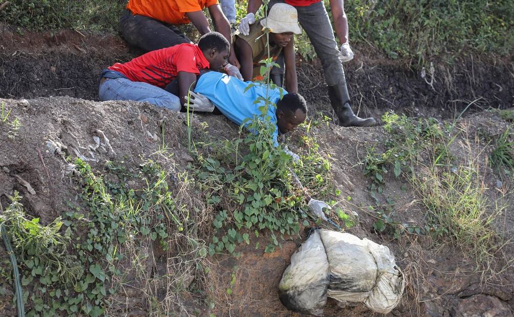 Un grupo de hombres recupera un cuerpo envuelto en una bolsa del interior de una cantera convertida en vertedero en la zona de Embakasi en Nairobi. Foto: EFE