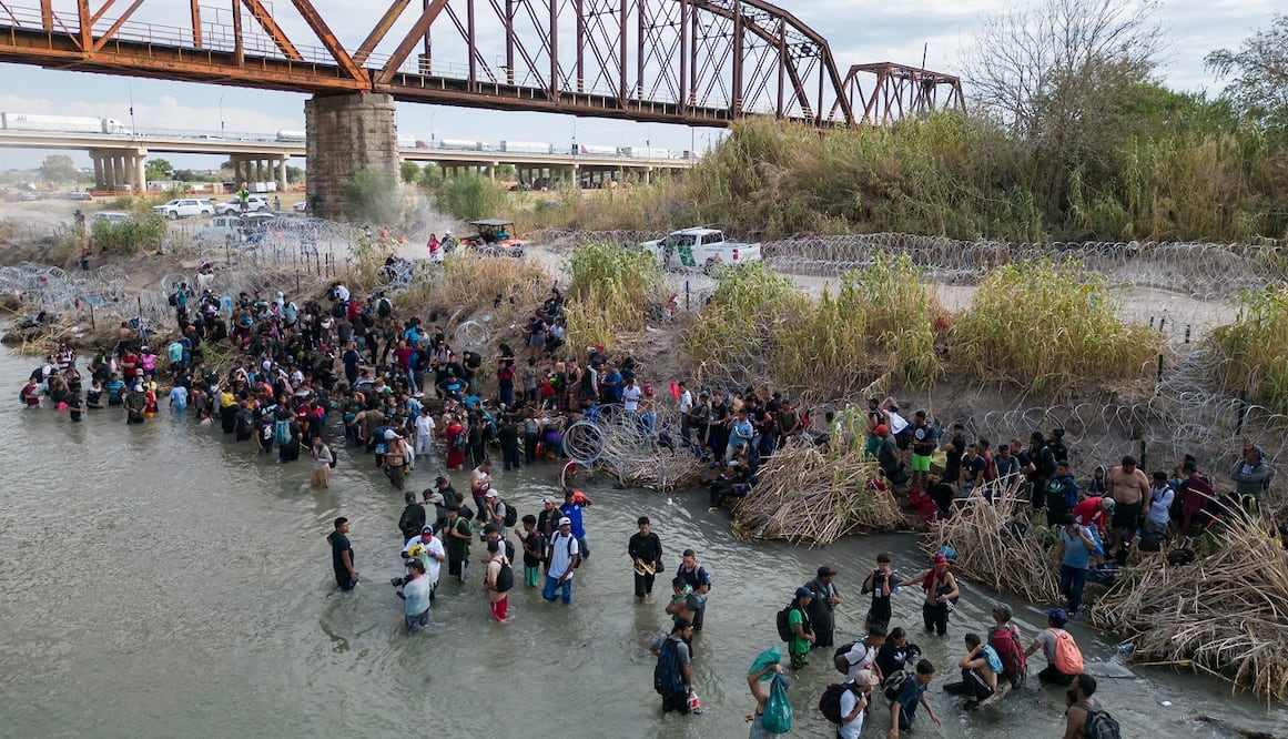 Foto aérea que muestra a los migrantes esperando en el Río Grande a que corten la alambrada de púas para poder cruzar hacia Eagle Pass, en Texas. FOTO: AFP