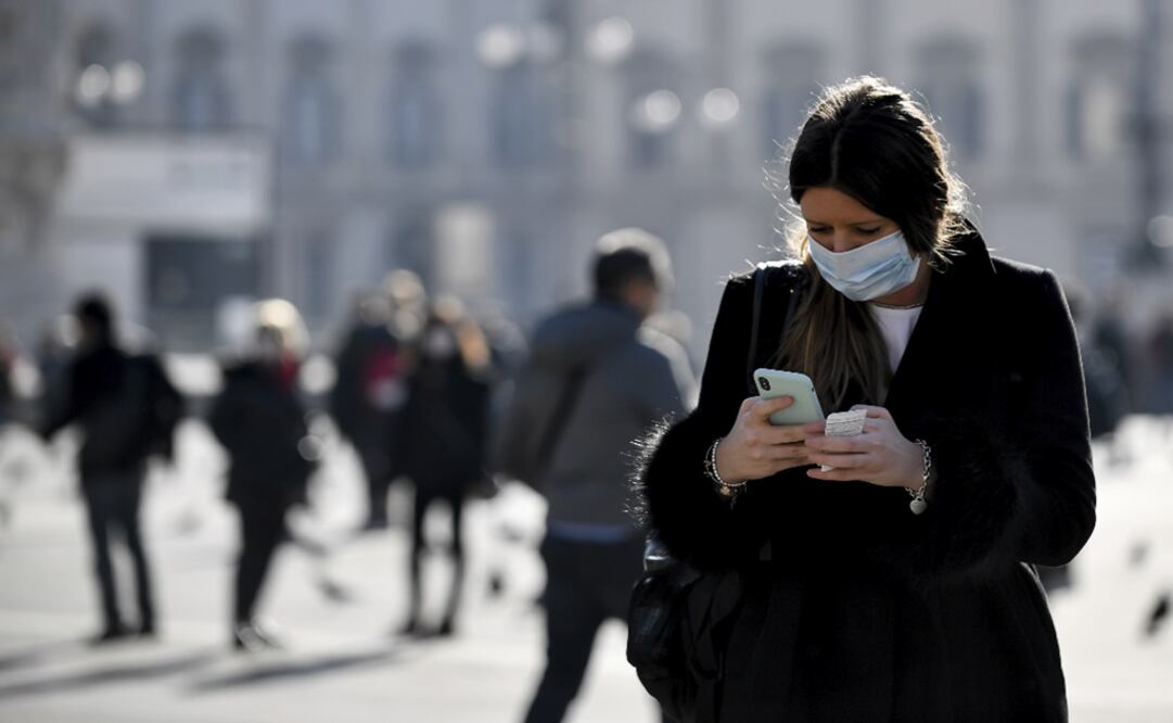 A woman wearing a sanitary mask looks at her phone - Photo: Claudio Furlan/Lapresse via AP