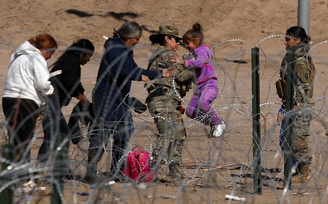 Un agente de la Guardia Nacional de Texas lleva a una niña migrante sobre una valla de púas en las orillas del Río Grande en El Paso, Texas, en la frontera con Ciudad Juárez. HERIKA MARTÍNEZ. AFP