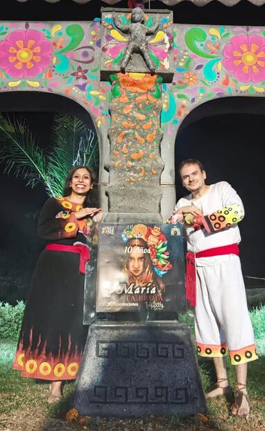 Los actores Alicia Lara, como la bruja mayor y Rodrigo Carbajal, en el papel de Juan, hermano de Santiago, posaron junto a la placa de las 100 representaciones. Rodrigo ha participado en la obra durante estos 10 años. Crédito: Producción La bruja Tlahuipochi/Cortesía.