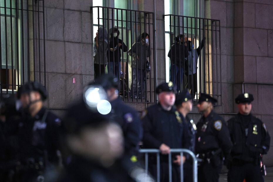Los estudiantes miran desde una ventana mientras los agentes de la policía de Nueva York hacen guardia frente a la Universidad de Columbia en la ciudad de Nueva York el 30 de abril de 2024. Foto: CHARLY TRIBALLEAU / AFP