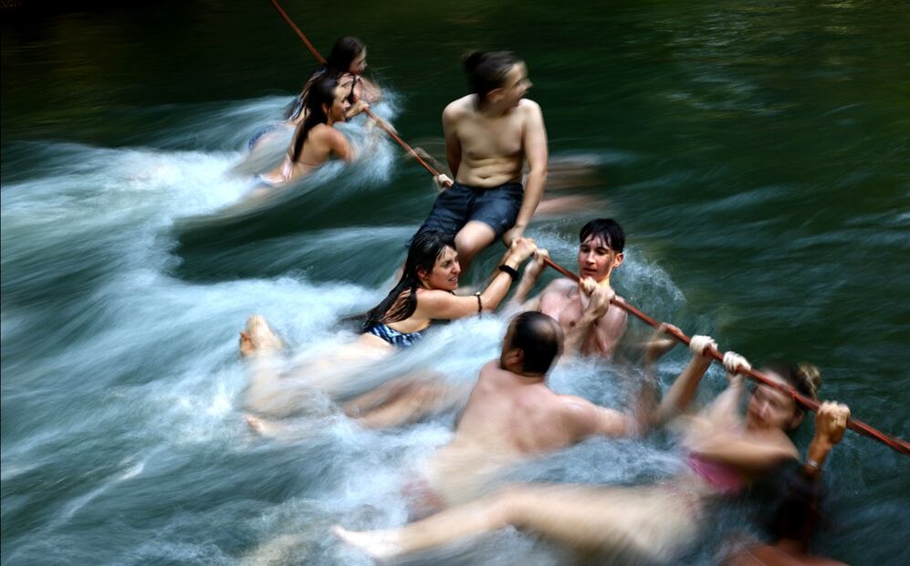 Varias personas se cuelgan de una cuerda en el arroyo Eisbach en el Jardín Inglés en Múnich, Alemania (01/07/2025). El Servicio Meteorológico alemán alertó de una ola de calor con temperaturas que alcanzarán los 38 grados centígrados en gran parte del país. Foto: EFE