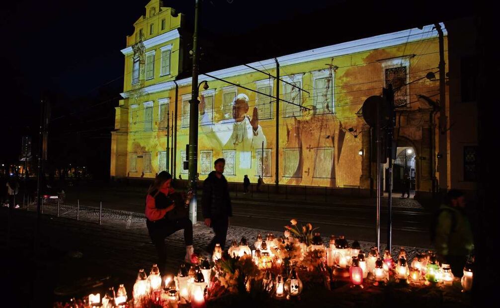 Fieles encienden velas ante las iluminaciones que representan a Juan Pablo II en el Palacio Episcopal de la calle Franciszkanska en Cracovia, Polonia. (14/04/2025) Foto: Lukasz Gagulski | EFE