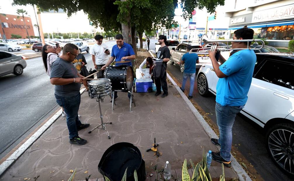 En la imagen se aprecia a un grupo de músicos de banda sinaloense que tocan en las calles a cambio de una propina porque les han cancelado las presentaciones nocturnas. A la derecha se lee un mensaje improvisado de un restaurante que da la bienvenida a los desayunos como modelo de adaptación de ventas / Foto: Diego Prado. EL UNIVERSAL