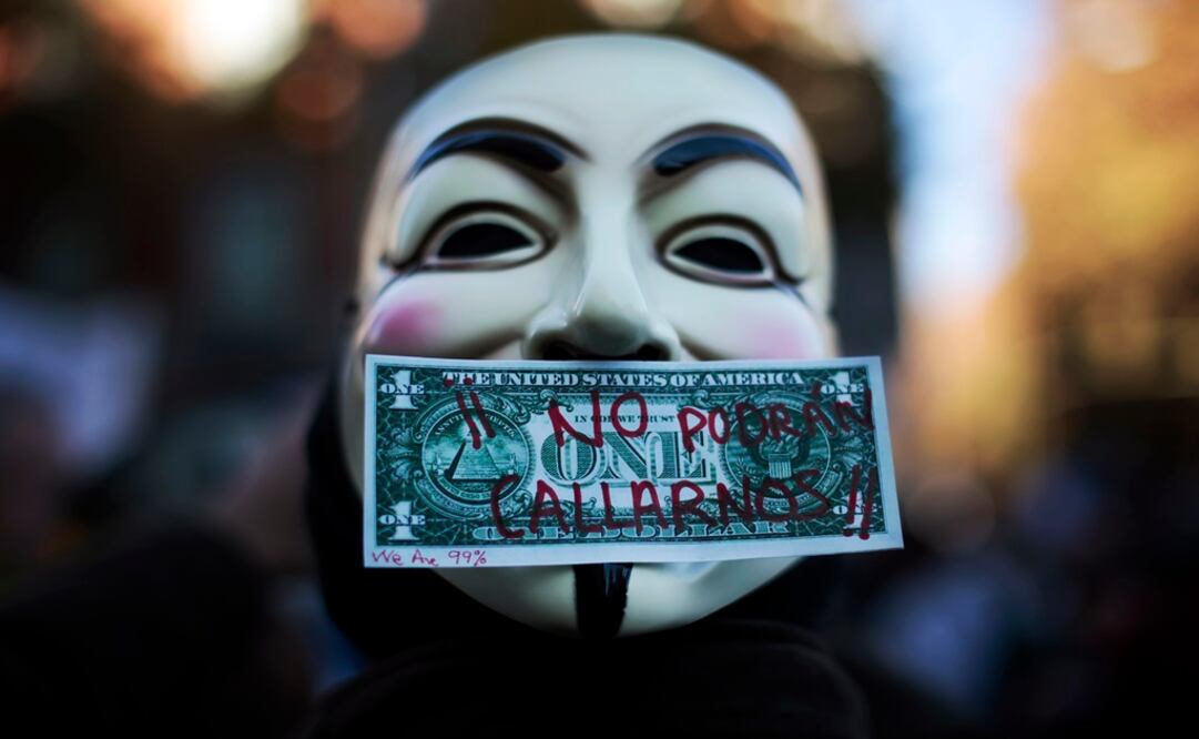 Protester wearing a Guy Fawkes mask is pictured with a fake dollar bill. The words on the bill read, "We won't be silenced" - Photo: Susana Vera/REUTERS