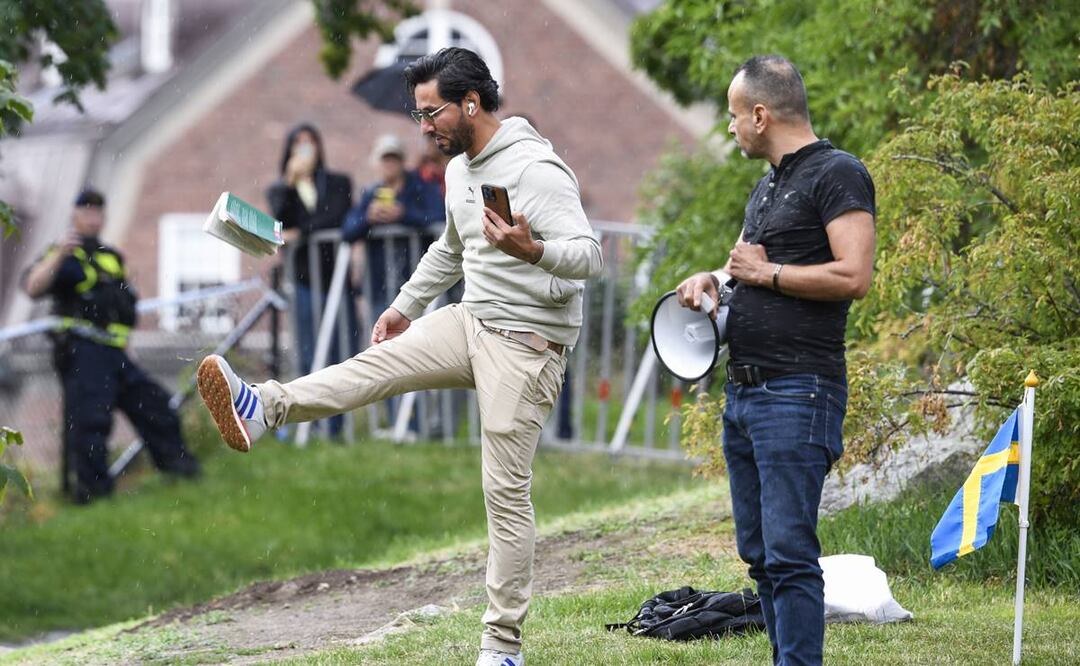 Un policía sueco observa al manifestante Salwan Momika (izquierda) mientras patea una copia del Corán durante su manifestación frente a la embajada iraquí en Estocolmo. Foto: EFE