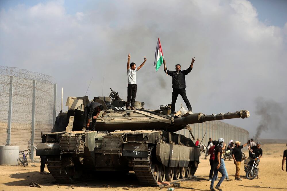 Los palestinos ondean su bandera nacional y celebran junto a un tanque israelí destruido en la valla de la Franja de Gaza al este de Khan Younis, al sur, el sábado 7 de octubre de 202. Foto: AP