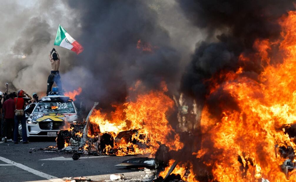 Un manifestante sostiene una bandera mexicana mientras coches en llamas se alinean en la calle el 8 de junio de 2025 en Los Ángeles, California. Foto: Mario Tama/Getty Images/AFP