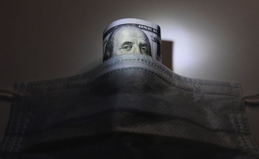 A U.S. dollar banknote is pictured behind a protective mask, which is widely used as a preventive measure against the coronavirus (COVID-19) - Photo: Alexey Pavlishak/REUTERS