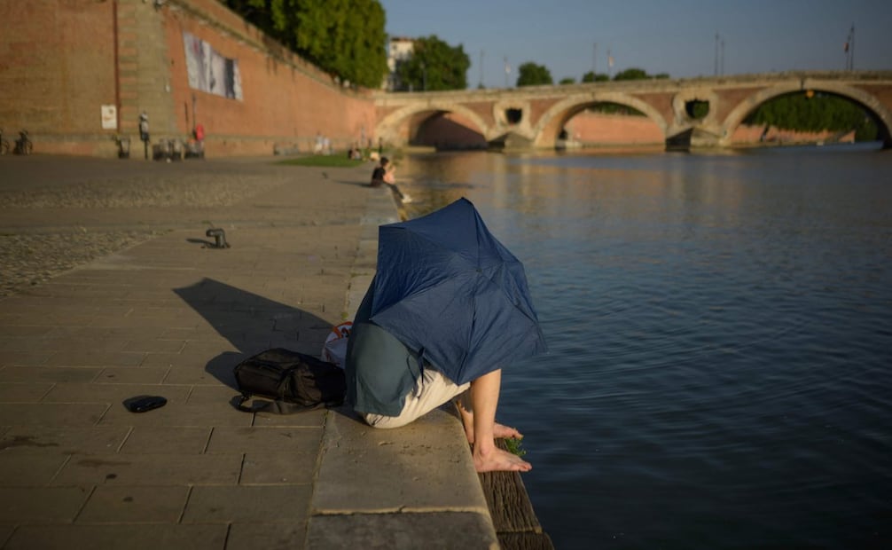 Un hombre se protege del sol bajo una sombrilla sentado junto al río Garona, en Toulouse, el 20 de junio de 2025. España y Portugal registraron temperaturas récord el 30 de junio de 2025, mientras que Italia y Francia se preparaban para varios días más de una ola de calor devastadora que ha azotado el sur de Europa y Gran Bretaña, provocando alertas sanitarias y de incendios forestales. Foto: AFP
