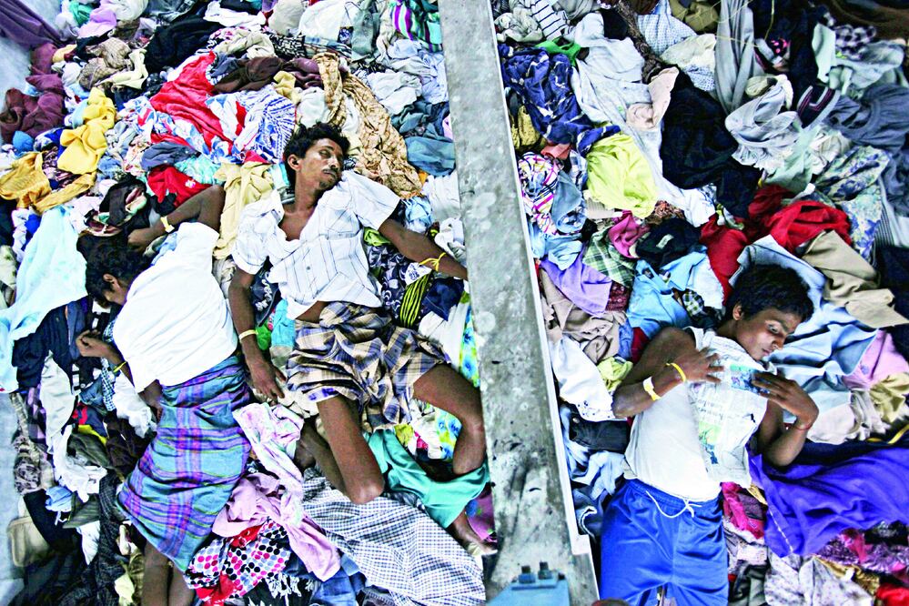 Hombres de etnia rohingya duermen una siesta sobre una pila de prendas de ropa donadas por residentes en un albergue temporal en Langsa, en la provincia indonesia de Aceh (BINSAR BAKKARA / AP)