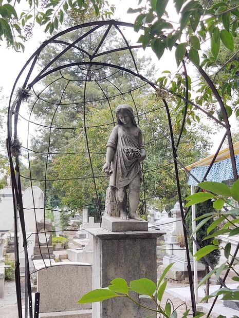 En esta tumba los deudos parecen haber preferido una lápida no muy grande que dejara espacio a la malla metálica, que podría haber sostenido una cúpula con plantas de enredadera, quizás a juego con el ramillete que sostiene la pequeña estatua. Foto: Alicia Vázquez.