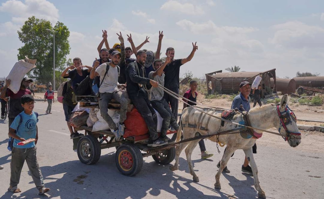 Palestinos saludan a la cámara mientras llevan paquetes de ayuda humanitaria cerca de un centro de distribución de la Fundación Humanitaria de Gaza, operado por la organización respaldada por Estados Unidos, en Netzarim, en el centro de la Franja de Gaza, el lunes 4 de agosto de 2025. Foto: AP