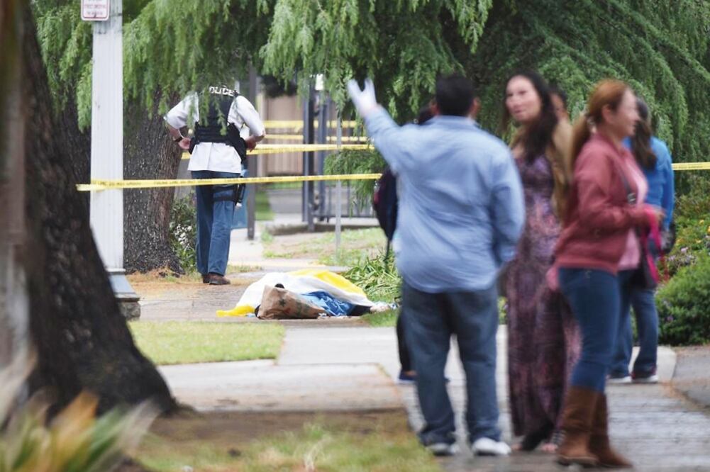 Trabajadores que fueron desalojados permanecieron cerca del sitio en el que estaba una víctima fatal del ataque a balazos sobre la acera de una calle de Fresno, California (AP)