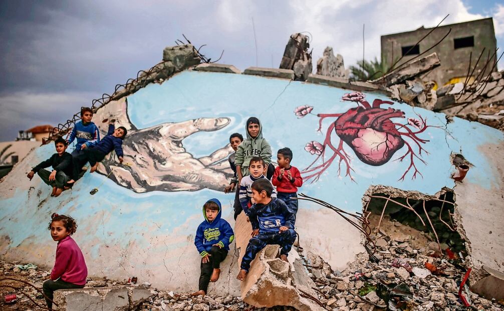 Niños palestinos desplazados juegan junto a un mural pintado en los escombros de una casa, en la localidad de Deir Al Balah, en la Franja de Gaza. Foto: EFE