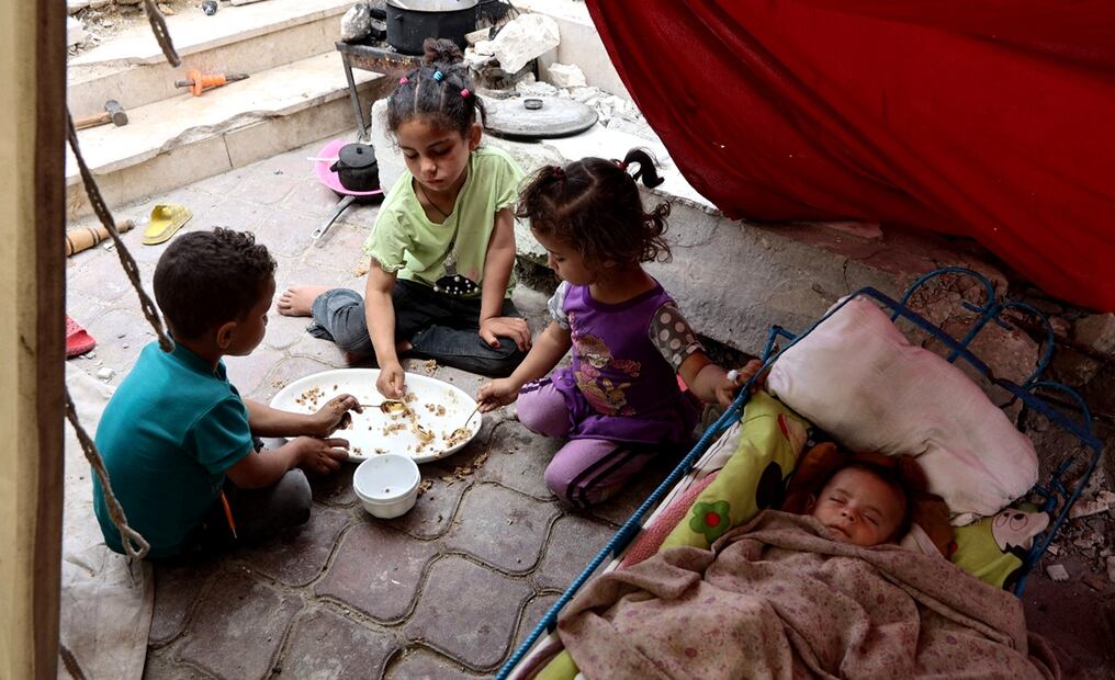 Niños palestinos comparten una comida de arroz mientras un bebé duerme, dentro de una tienda de campaña cerca del puerto de la ciudad de Gaza, el 22 de mayo de 2025. Foto: AFP