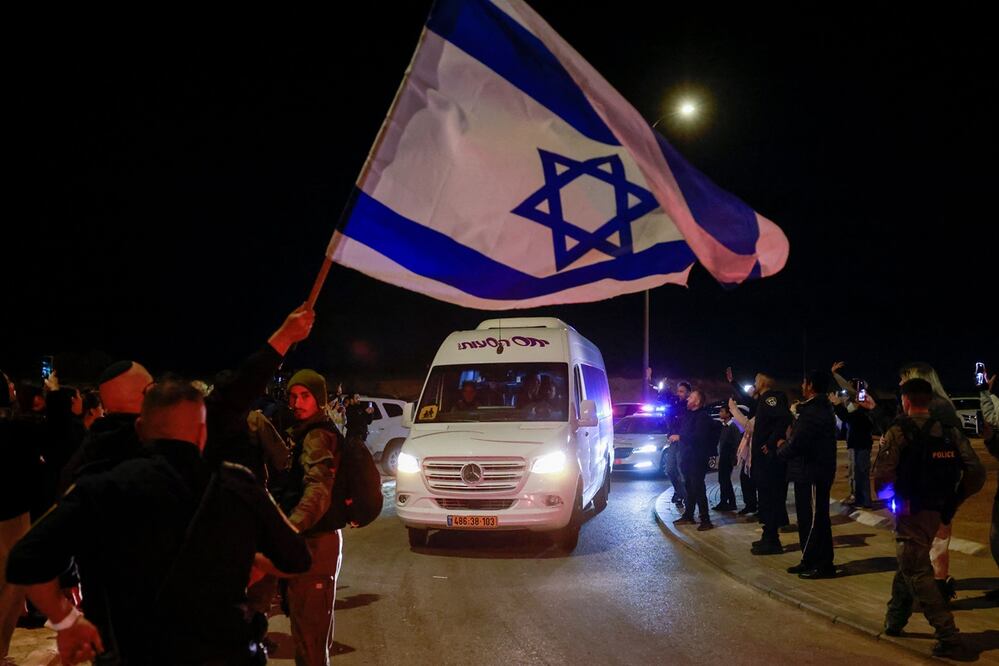 Un hombre ondea una bandera israelí mientras un vehículo que transporta a dos rehenes liberados por militantes de Hamas, el 29 de noviembre de 2023 pasa por Ofakim, en el sur de Israel. Foto: AFP