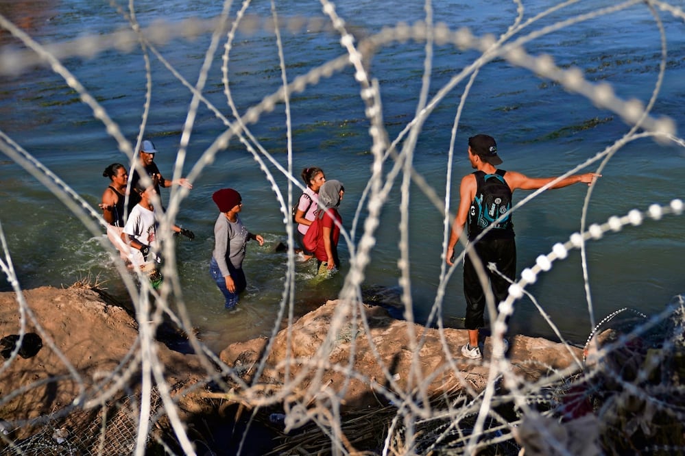 Indocumentados caminan por el río Grande a lo largo de un alambrado, mientras intentan cruzar a Estados Unidos desde México. Foto: Eric Gay. AP