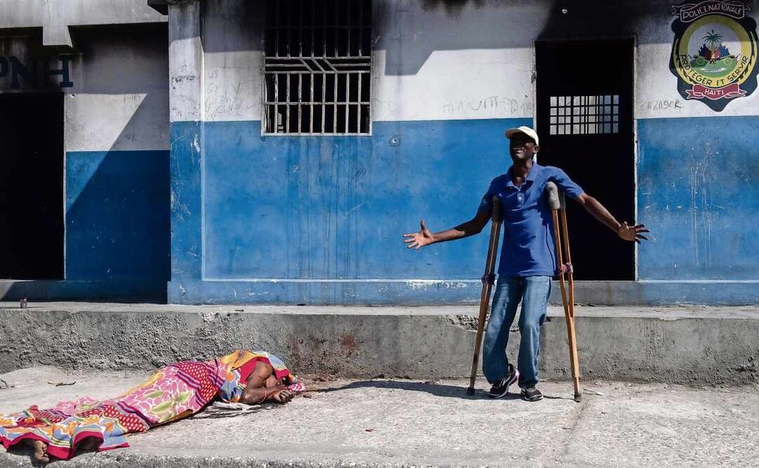 Un hombre, junto al cuerpo sin vida de una persona en los exteriores de la comisaría de Carrefour Aéroport, que fue incendiada la noche del 4 de marzo por miembros de pandillas, en Puerto Príncipe, Haití. Foto: Johnson Sabin / EFE