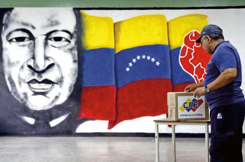 Un ciudadano emite su voto en un centro electoral, en Caracas, cuyo fondo tiene un mural de Hugo Chávez (FAUSTO TORREALBA. XINHUA)