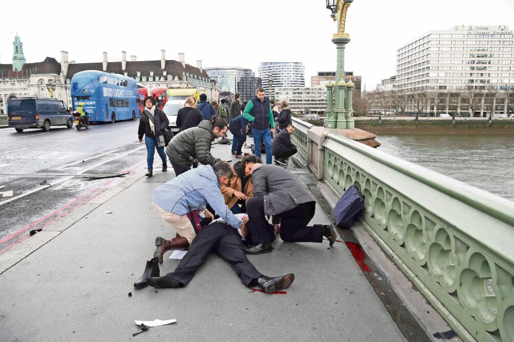 Un grupo de personas atiende a un hombre que resultó herido cuando un individuo en un vehículo arrolló a quienes se encontraban en la banqueta del puente de Westminster, a un costado del edificio del Parlamento (TOBY MELVILLE. REUTERS)