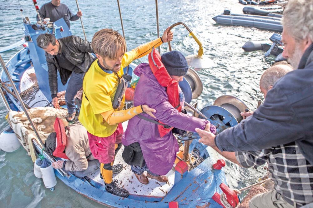 Un socorrista voluntario de la ONG española Open Arms, ayuda a desembarcar a un grupo de personas que trataba de cruzar el mar Egeo desde las costas turcas al norte de la isla griega de Lesbos (SANTI DONAIRE. EFE)