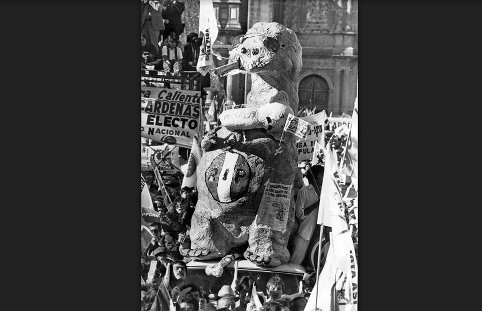 “Un dinosaurio de cartón con lentes oscuros y puro, así como un circulo tricolor con las iniciales del PRI invertidas, fue llevado al Zócalo capitalino por jóvenes cardenistas que apoyan a Cuauhtémoc Cárdenas”, indica el pie de foto de esta imagen captada durante las elecciones de 1988. Imagen: Archivo El Universal