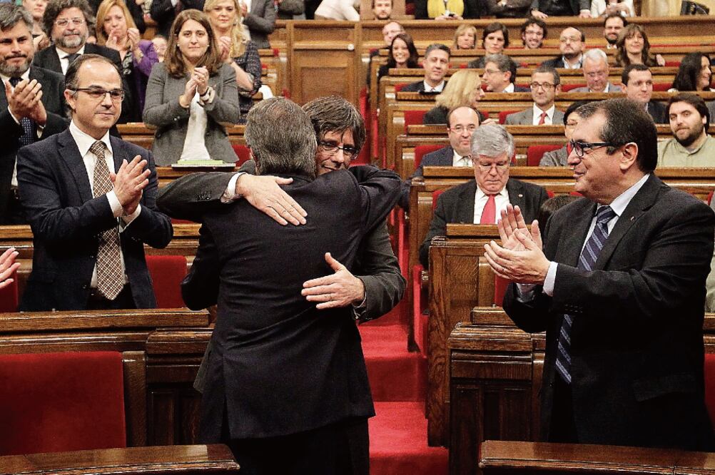 El líder catalán saliente, Artur Mas (de espaldas), abraza a Carles Puigdemo nt, nuevo presidente de la Generalitat, en el pleno del Parlamento, en Barcelona (ALBERTO ESTÉVEZ. EFE)