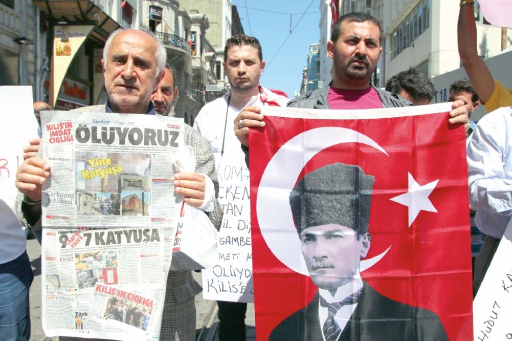 Turcos sostienen una imagen de Kemal Ataturk, fundador del país, y un periódico que dice: “S.O.S desde Kilis: estamos muriendo”, una zona que ha sido atacada frecuentemente por proyectiles en las últimas semanas, por su cercanía con Siria (AP)