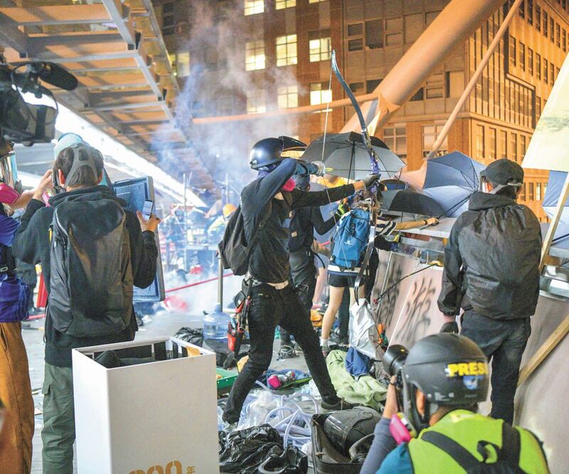 Un manifestante se prepara para disparar una flecha mientras la policía repele la protesta con gas lacrimógeno en la Universidad Politécnica de Hong Kong. Foto/ANTHONY WALLACE. AFP