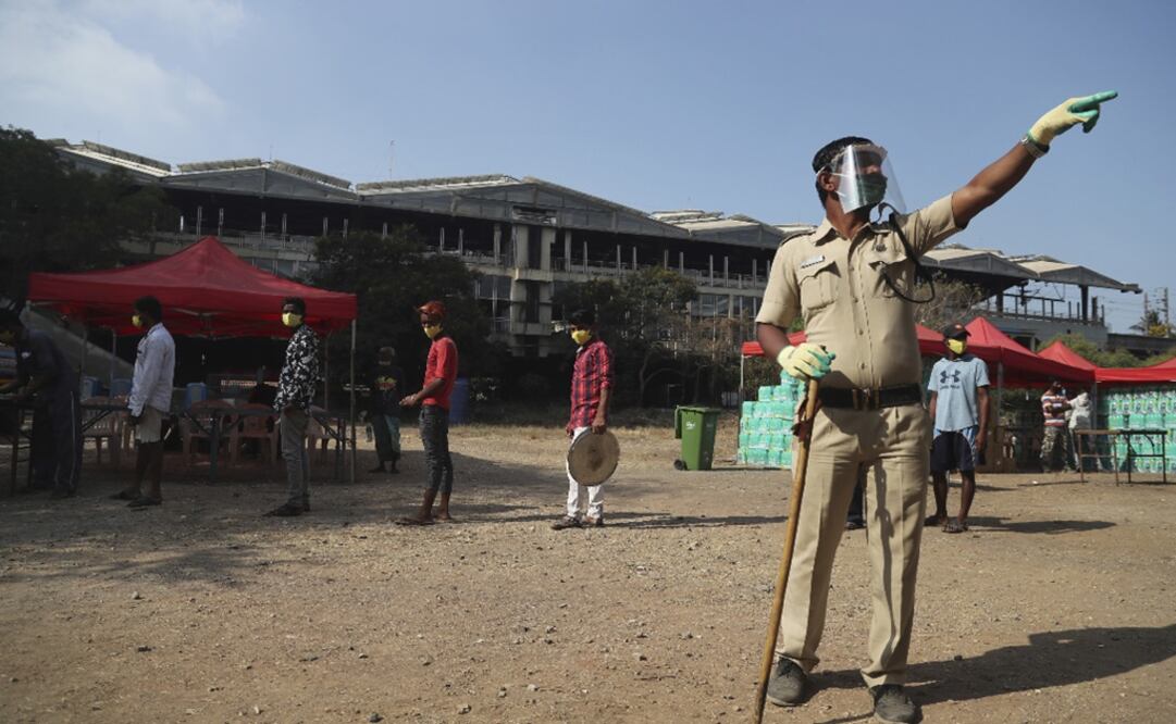 An India policeman stands guard as people queue up for breakfast at a shelter – Photo: Rafiq Maqbool/AFP