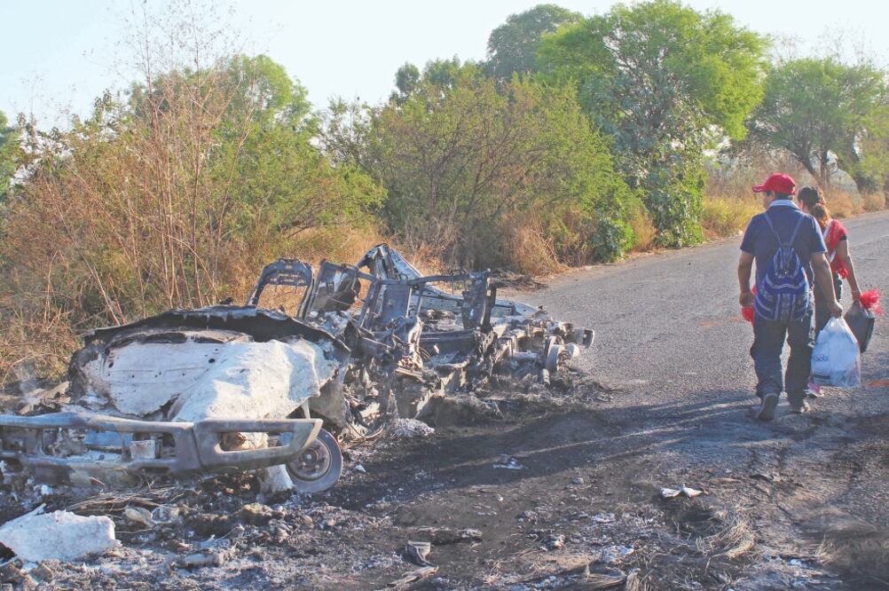 Dos personas pasan junto a un auto incendiado en uno de los caminos bloqueados hacia Santa Rosa de Lima, en Guanajuato. Foto: ALEJANDRO ROJAS. CUARTOSCURO