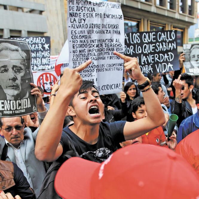 Ciudadanos colombianos con letreros contra Álvaro Uribe, expresidente y legislador de Colombia, protestaron mientras el senador asistía a una audiencia privada en la Corte Suprema de Justicia.  REUTERS