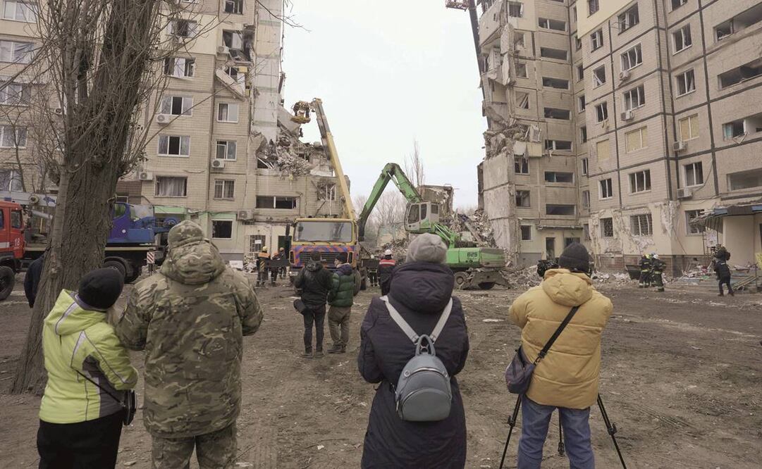 Ucranianos ven cómo rescatistas trabajan en un edificio residencial destruido durante un ataque con misiles, en la localidad de Dnipro. 