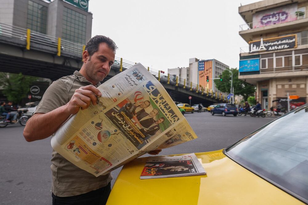 Un iraní lee un periódico en una calle de Teherán el 12 de abril de 2025. La portada presenta las conversaciones entre Irán y Estados Unidos sobre el programa nuclear iraní, que comenzarán en Omán ese mismo día.  Foto: AFP