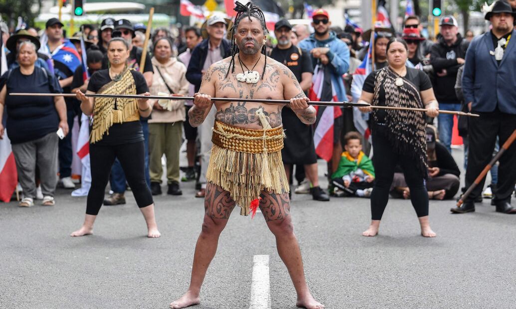 Hombres tatuados con el torso desnudo, enarbolando la bandera roja, blanca y negra de los maoríes participaron en la marcha (18/11/2024). Foto: Sanka Vidanagama / AFP