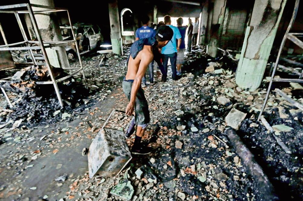 De entre los escombros. Civiles se llevan objetos que quedaron tras el incendio intencional de una casa en el que fallecieron seis personas de una familia. (AFP)