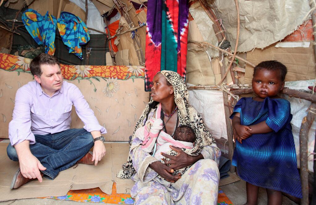 Imagen de 2012 que muestra a Justin Forsyth, entonces director de la organización británica Save The Children, habla con una desplazada somalí que carga a un bebé en brazos (Foto: Reuters)