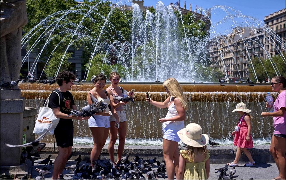 Turistas se acercan a una fuente mientras alimentan palomas en un día caluroso en Barcelona, España, el miércoles 2 de julio de 2025. Foto: AP